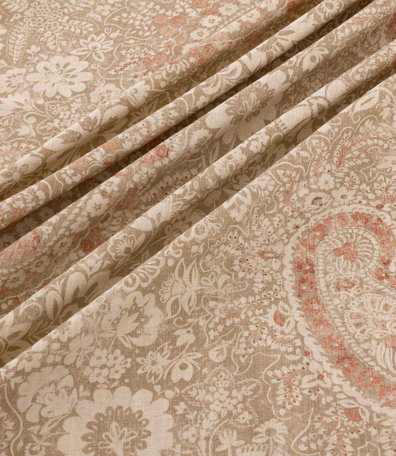 Southold Coralee fabric draped in soft diagonal folds, showcasing its detailed coral pink and cream paisley floral pattern, trailing botanical motifs, natural beige background and textured woven-look finish.