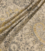 Southold Rockport fabric draped in soft diagonal folds, showcasing its detailed charcoal grey, olive and mustard yellow paisley floral pattern, trailing botanical foliage and textured natural cream background.