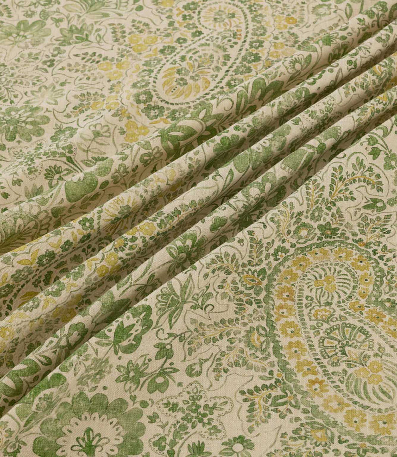 Southold Spring fabric draped in soft diagonal folds, showcasing its detailed green and yellow paisley floral pattern, delicate trailing foliage and textured cream background, with the folds highlighting the fabric's natural drape and intricate design.