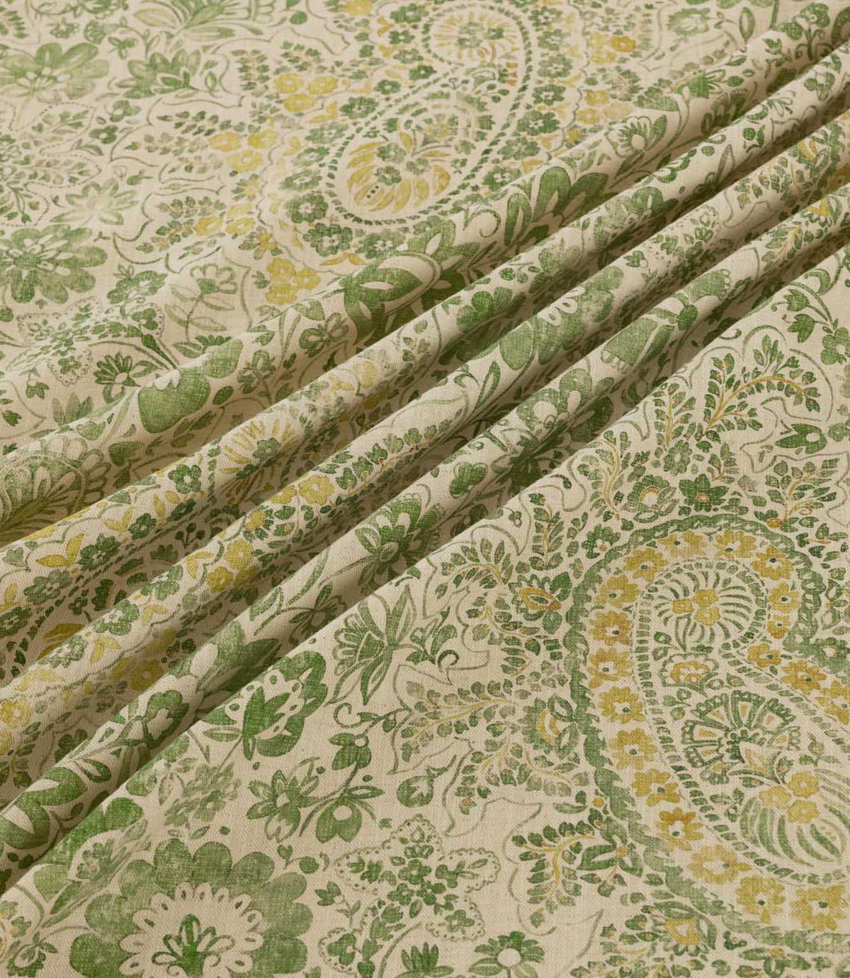 Southold Spring fabric draped in soft diagonal folds, showcasing its detailed green and yellow paisley floral pattern, delicate trailing foliage and textured cream background, with the folds highlighting the fabric's natural drape and intricate design.