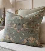 Decorative William Morris cushion with floral, strawberry and bird pattern fabric on a bed.