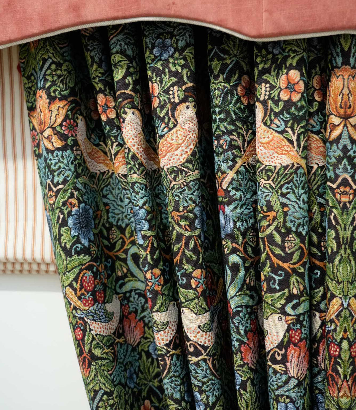 Strawberry Thief Tapestry Noir fabric made into gathered curtains, featuring birds, strawberries, flowers and dense green foliage on a dark background, styled beneath a rust pelmet.