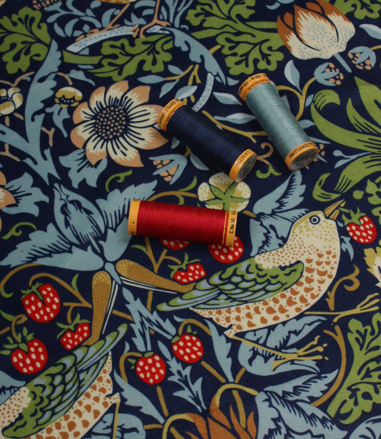 Spools of thread on a velvet William Morris fabric with floral, strawberry and bird pattern