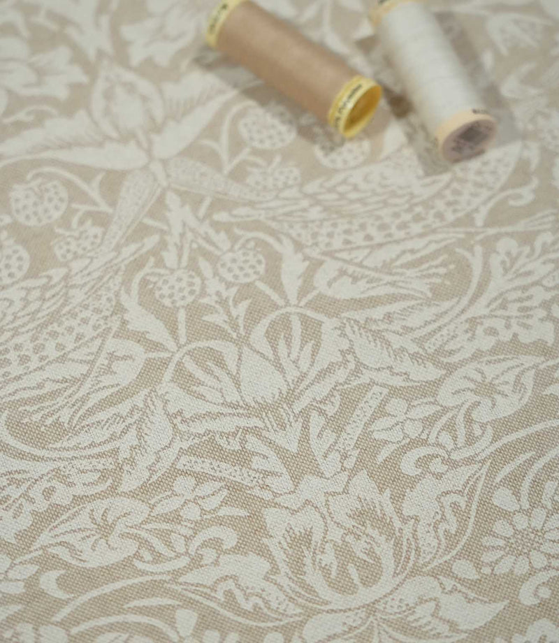 Strawberry Thief Linen Look fabric in beige and off-white with sewing threads, showing birds, strawberries and botanical details across the textured weave.