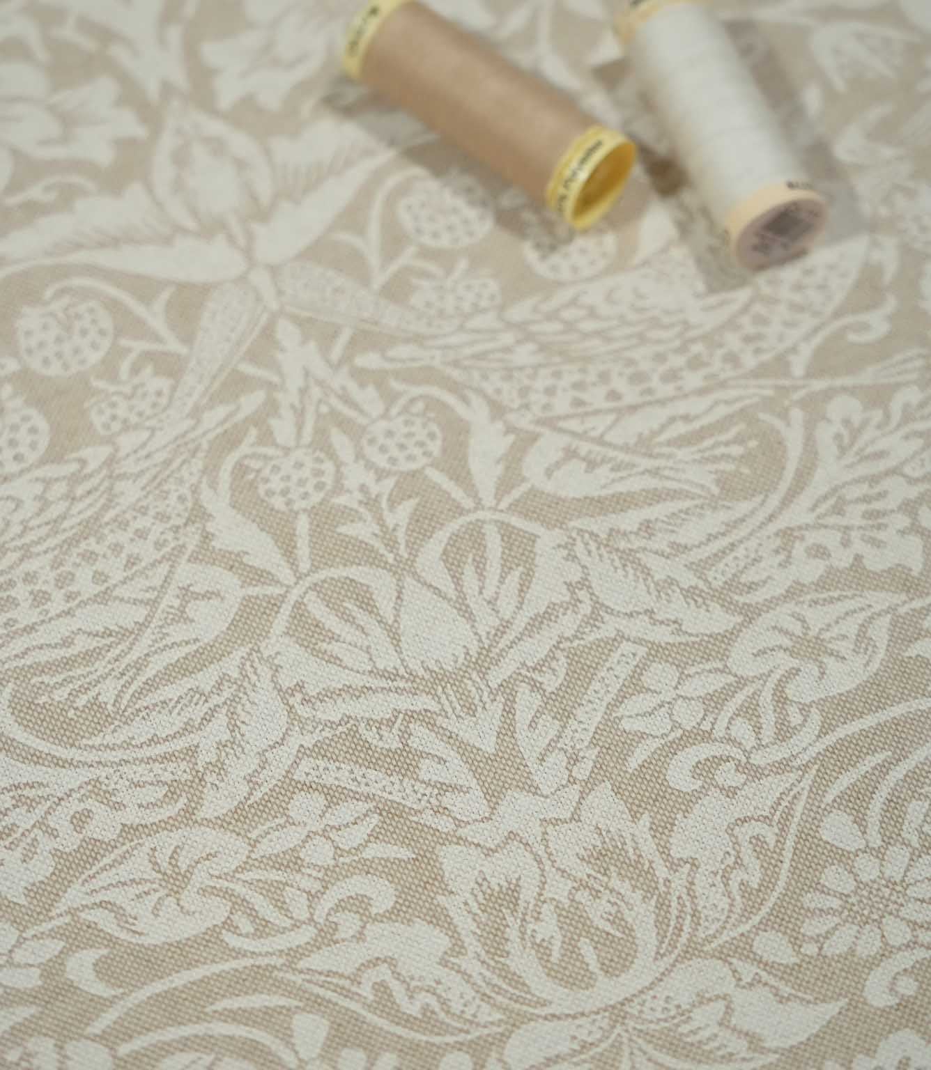 Strawberry Thief Linen Look fabric in beige and off-white with sewing threads, showing birds, strawberries and botanical details across the textured weave.