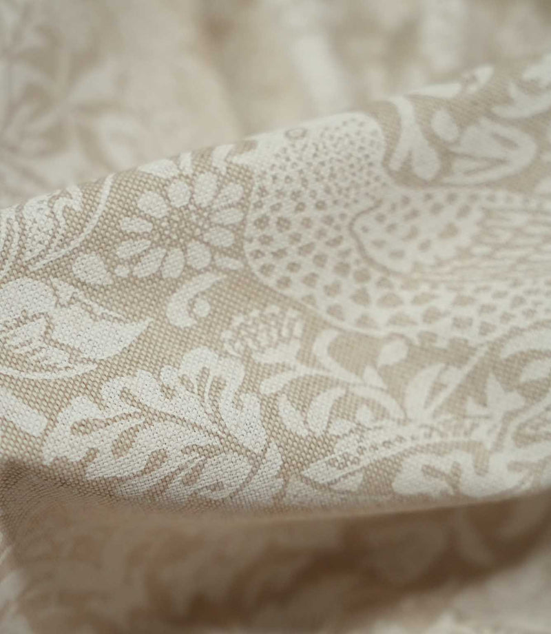 Close-up of draped Strawberry Thief Linen Look fabric in beige and off-white, highlighting the linen-look weave and detailed William Morris bird and botanical motifs.