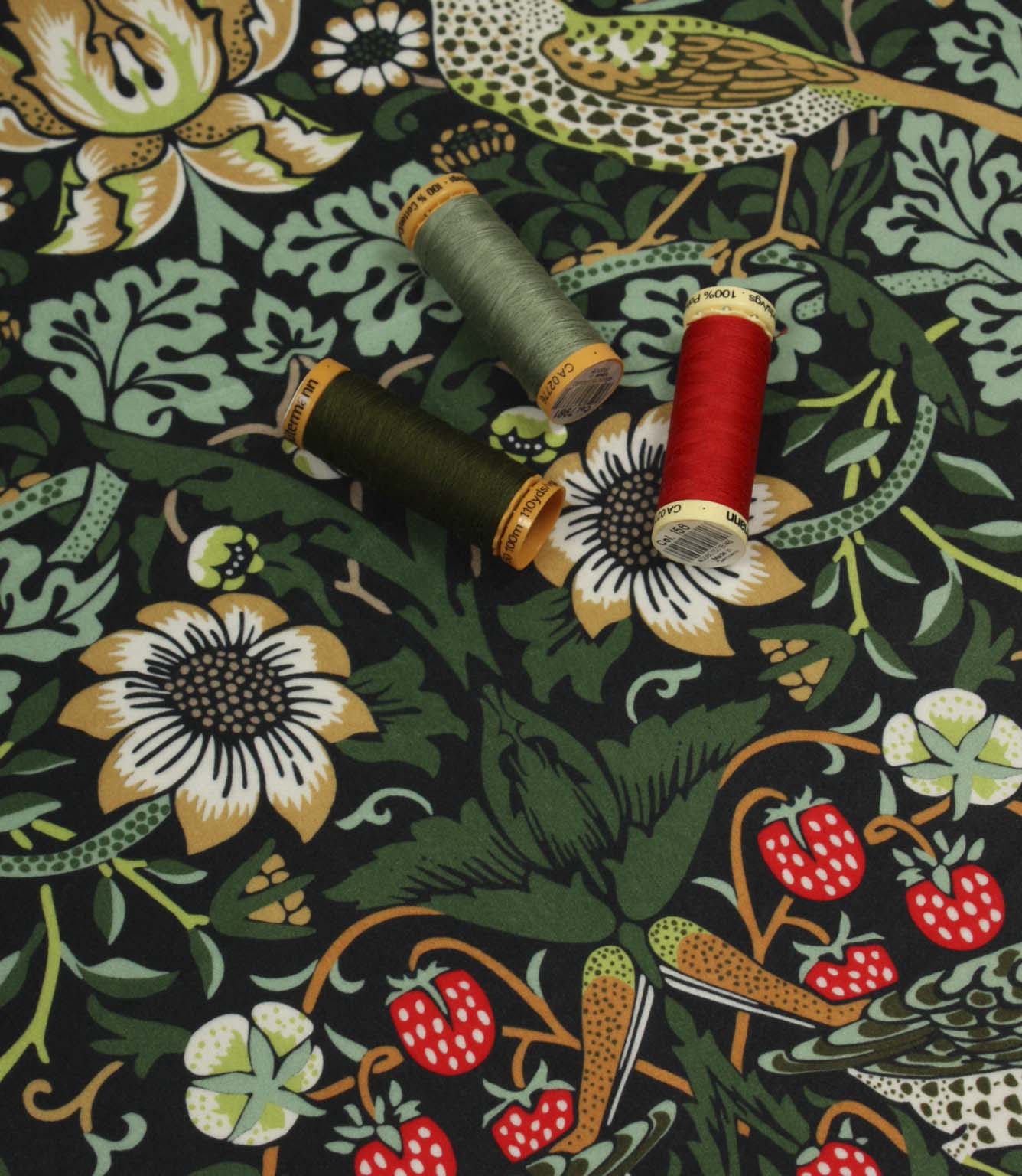 Black floral and bird print fabric shown with coordinating thread reels in green, mint and red tones.
