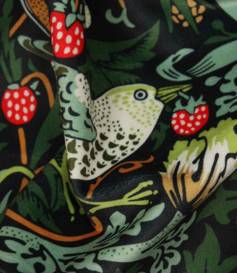 Detailed close-up of bird motif on black botanical fabric with bright red strawberries and soft green leaves.