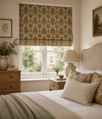 Warm, softly lit bedroom with floral Roman blinds in sage green, mustard and coral tones. Neutral bedding, gingham accent cushion, wooden furniture and botanical décor create a calm, rustic cottage-style interior.