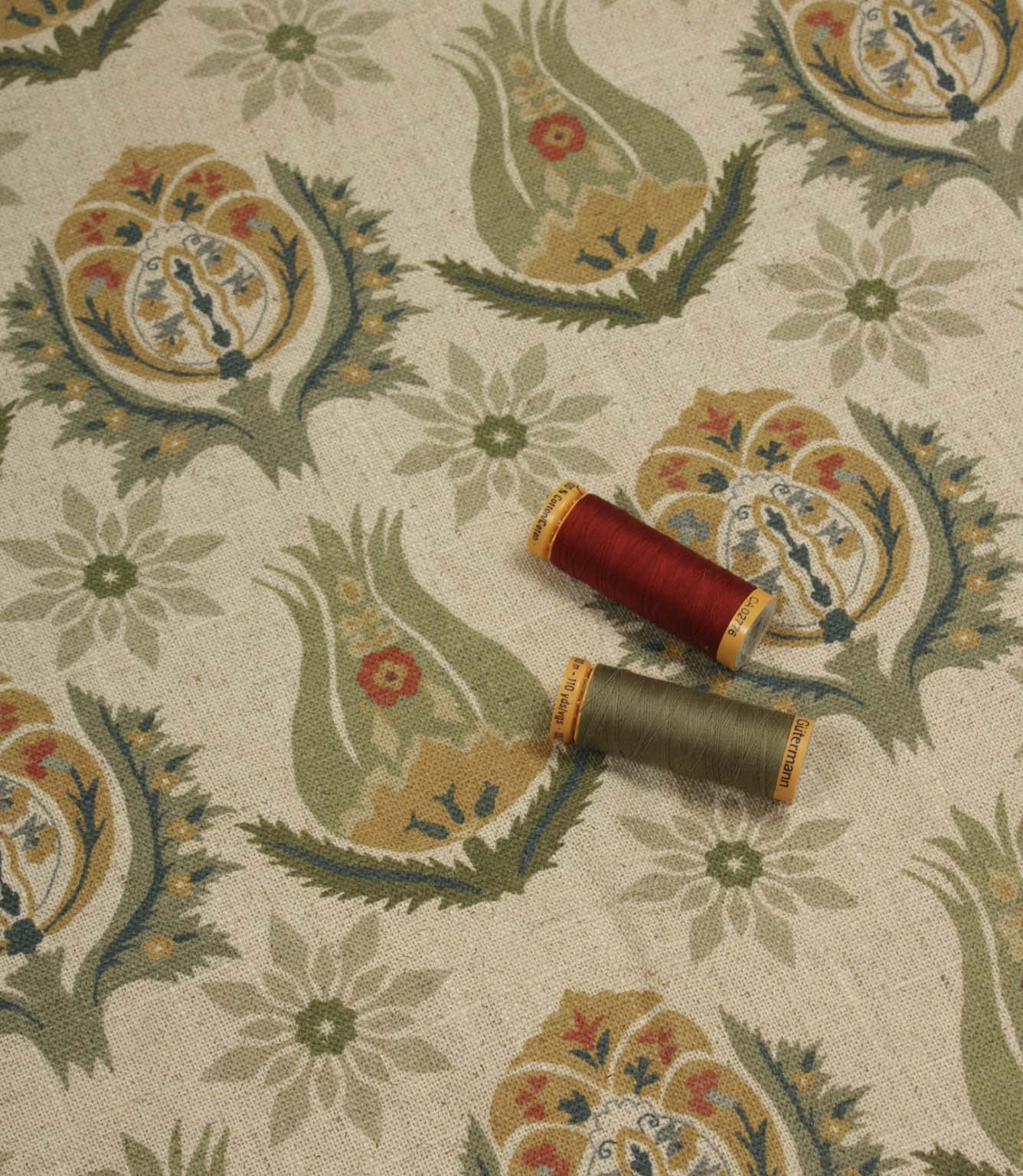 Natural linen-style floral fabric displayed with coordinating olive and red thread reels.