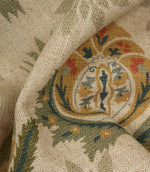 Detailed close-up of textured woven fabric featuring intricate floral medallion design in sage green, ochre and muted red colours.