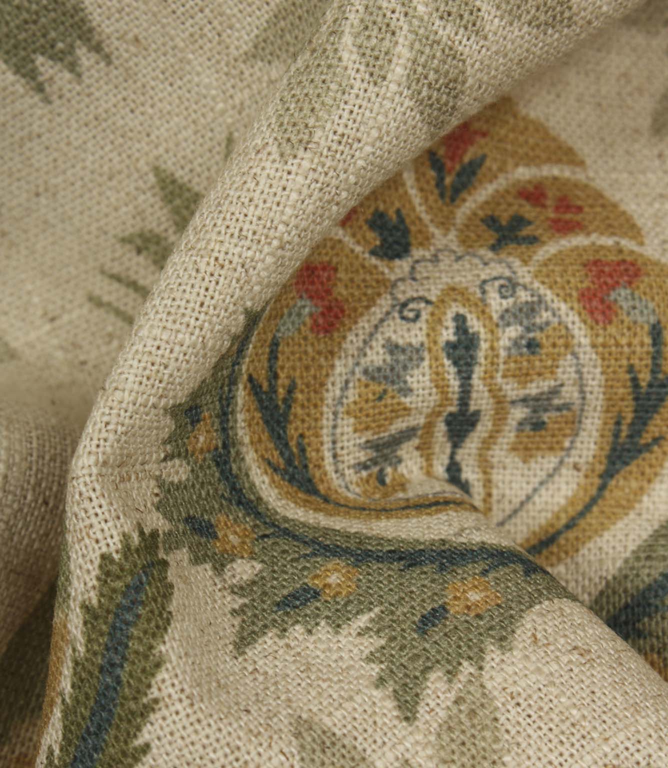 Detailed close-up of textured woven fabric featuring intricate floral medallion design in sage green, ochre and muted red colours.