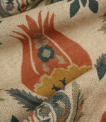Detailed close-up of textured woven fabric with large stylised floral motif in rust red, mustard and deep blue colours.