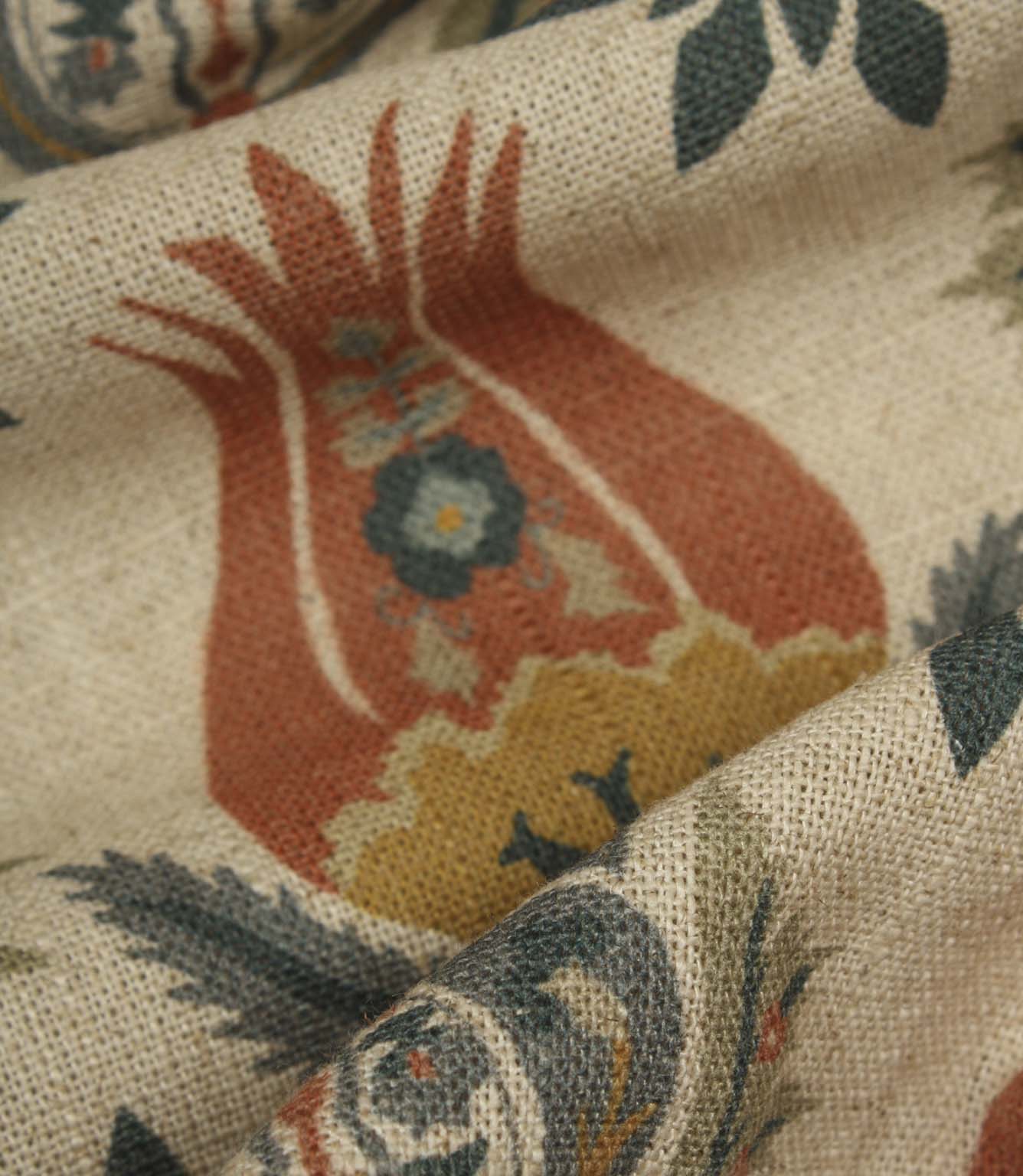 Detailed close-up of textured woven fabric with large stylised floral motif in rust red, mustard and deep blue colours.