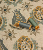 Decorative botanical fabric shown with coordinating sage green and blue thread reels on a natural linen-look ground.