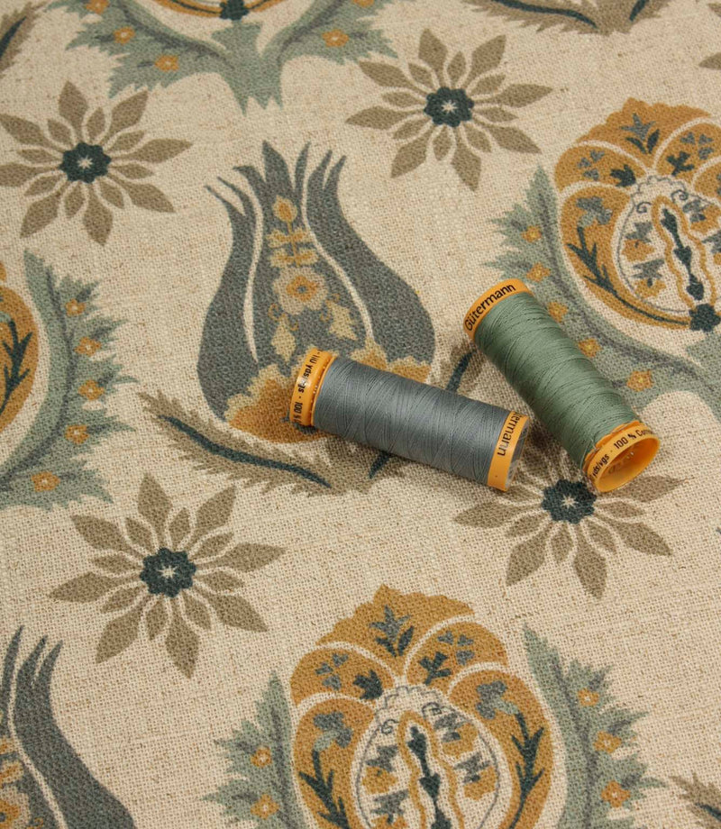 Decorative botanical fabric shown with coordinating sage green and blue thread reels on a natural linen-look ground.