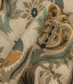 Detailed close-up of textured woven fabric highlighting ornamental floral design in muted blue and ochre tones.