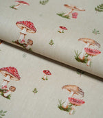 Toadstool Meadow Multi fabric folded over itself, displaying red spotted toadstools, brown mushrooms and delicate green woodland foliage across a natural beige textured background.