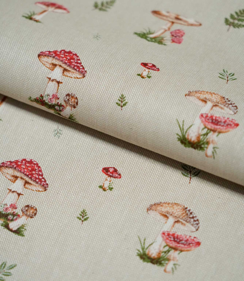 Toadstool Meadow Multi fabric folded over itself, displaying red spotted toadstools, brown mushrooms and delicate green woodland foliage across a natural beige textured background.
