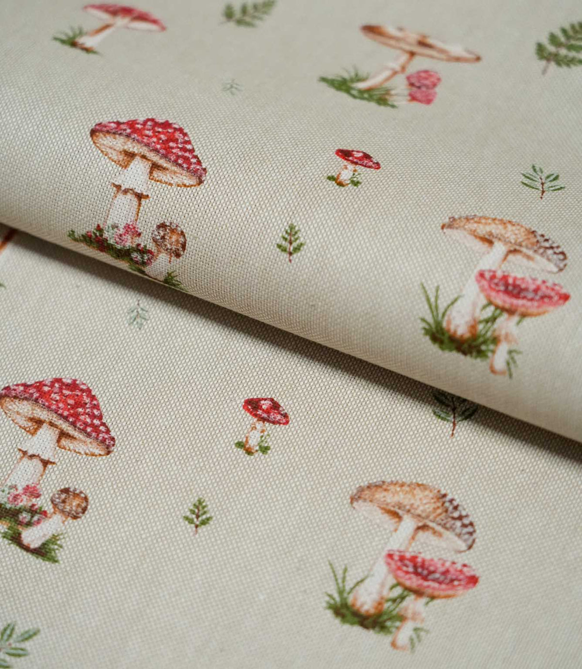 Toadstool Meadow Multi fabric folded over itself, displaying red spotted toadstools, brown mushrooms and delicate green woodland foliage across a natural beige textured background.