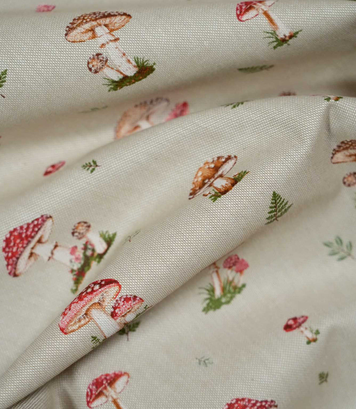 Toadstool Meadow Multi fabric loosely draped into soft folds, showing its natural beige woven texture and scattered red spotted toadstools, brown mushrooms and delicate green foliage.