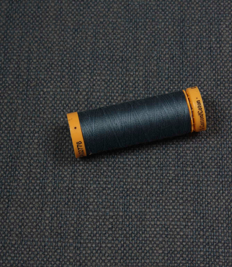 Trento woven plain fabric in indigo with coordinating thread spool, demonstrating the fabric's texture, weave and colour match.