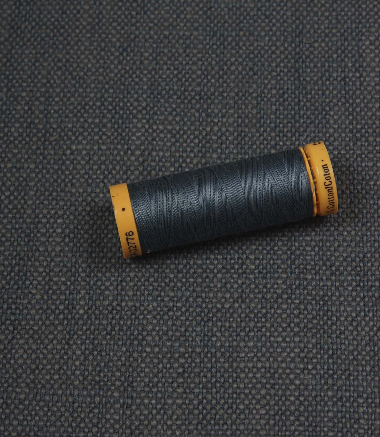 Trento woven plain fabric in indigo with coordinating thread spool, demonstrating the fabric's texture, weave and colour match.