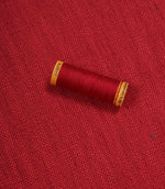 Trento woven plain fabric in peony with coordinating thread spool, demonstrating the fabric's texture, weave and colour match.