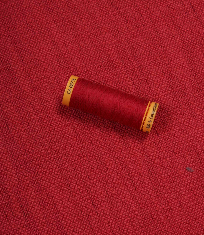 Trento woven plain fabric in peony with coordinating thread spool, demonstrating the fabric's texture, weave and colour match.