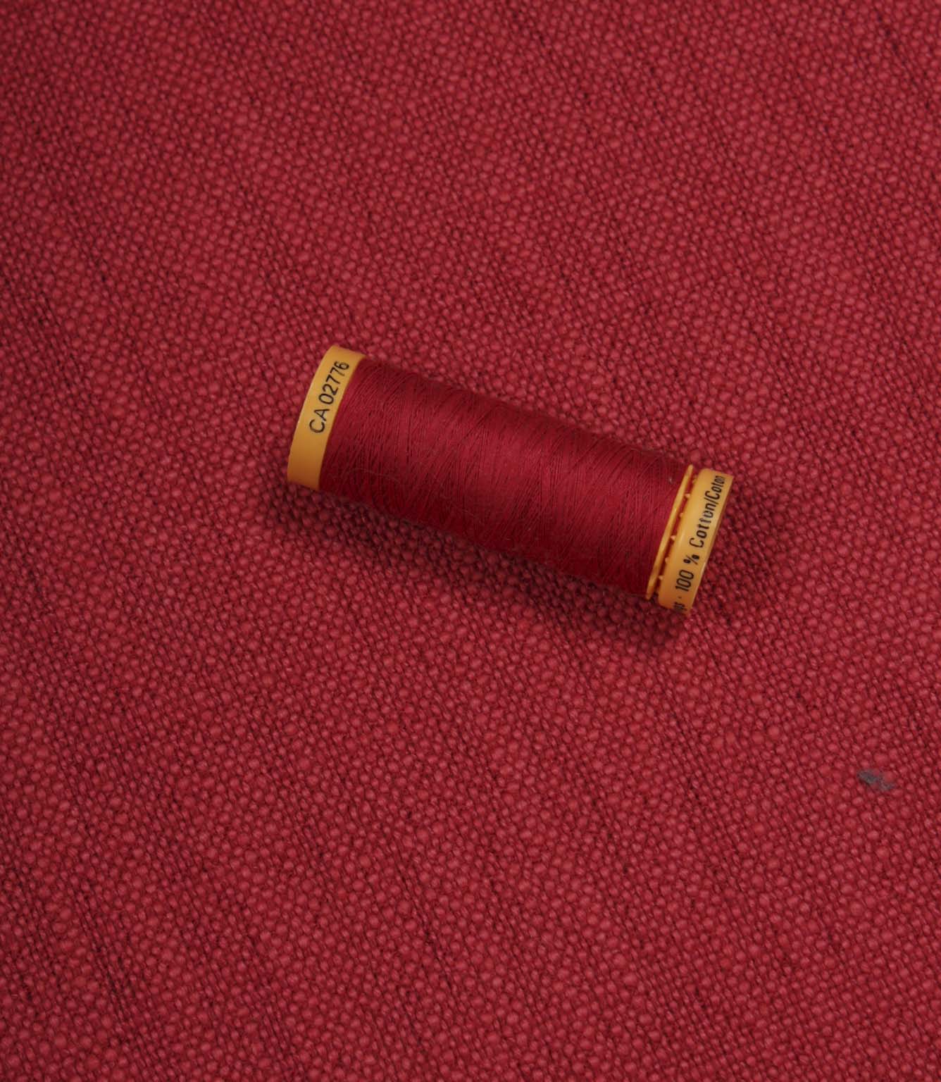 Trento woven plain fabric in peony with coordinating thread spool, demonstrating the fabric's texture, weave and colour match.