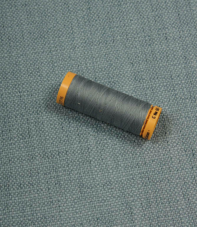 Trento woven plain fabric in sky with coordinating thread spool, demonstrating the fabric's texture, weave and colour match.