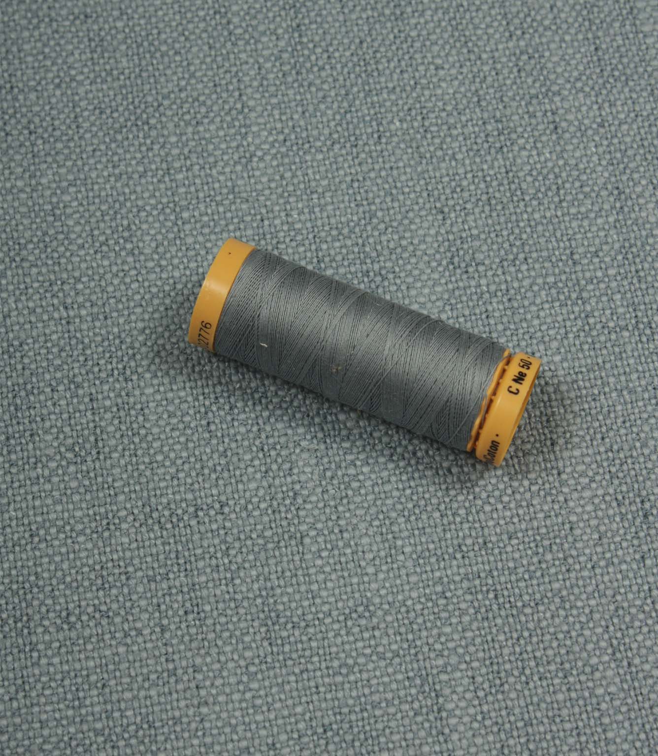 Trento woven plain fabric in sky with coordinating thread spool, demonstrating the fabric's texture, weave and colour match.