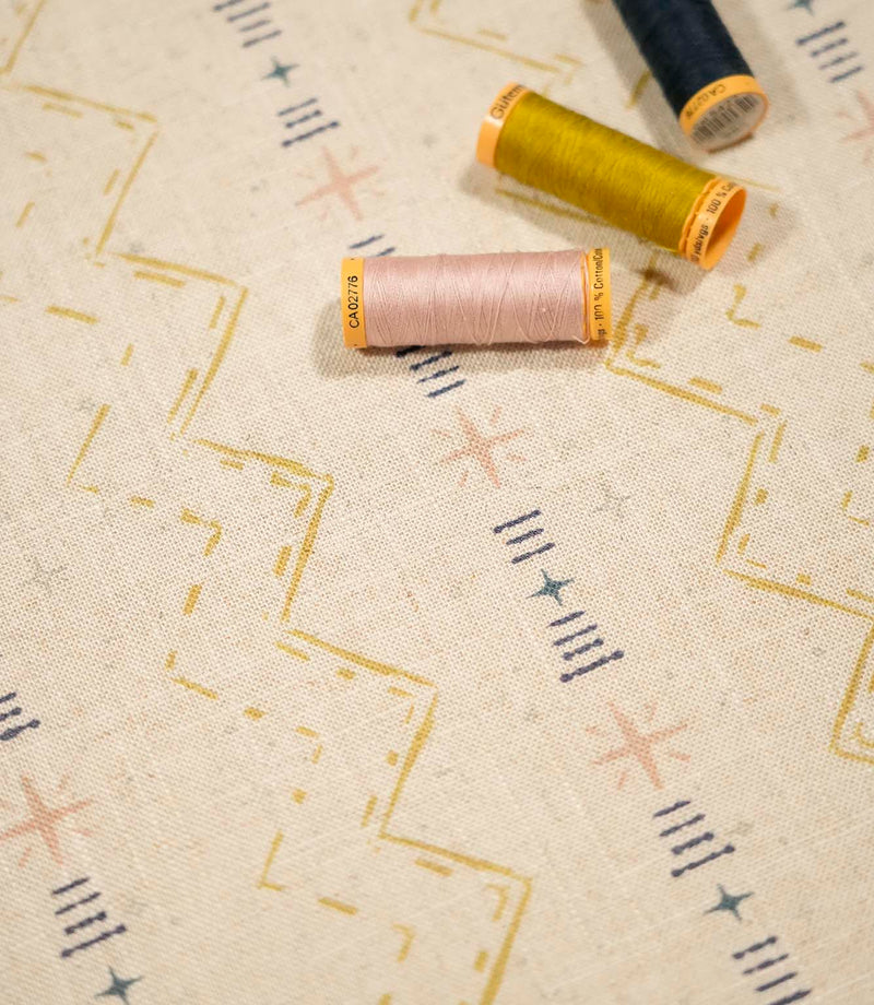Twilight Mill Gold fabric displayed with coordinating gold, blush and navy sewing thread, highlighting the contemporary geometric print.