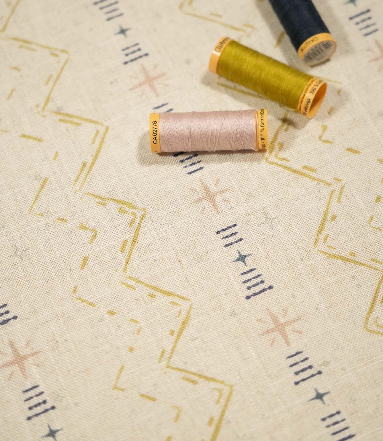 Twilight Mill Gold fabric displayed with coordinating gold, blush and navy sewing thread, highlighting the contemporary geometric print.