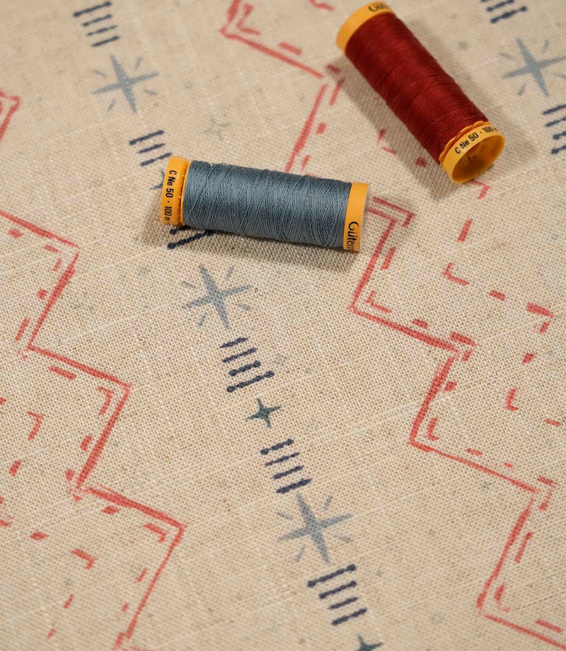 Twilight Mill Red Steel Blue fabric displayed with coordinating red and steel blue thread reels, highlighting the contemporary geometric design.