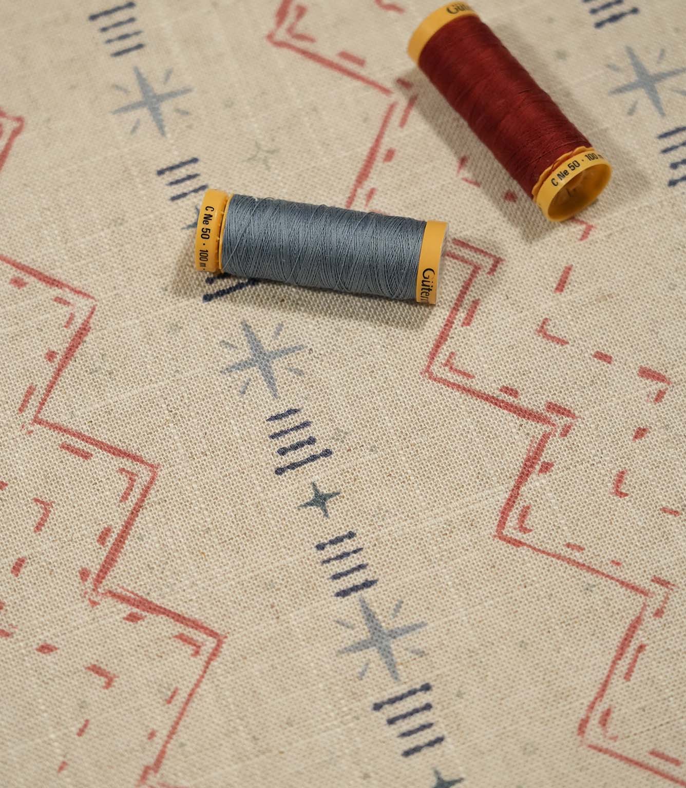 Twilight Mill Red Steel Blue fabric displayed with coordinating red and steel blue thread reels, highlighting the contemporary geometric design.