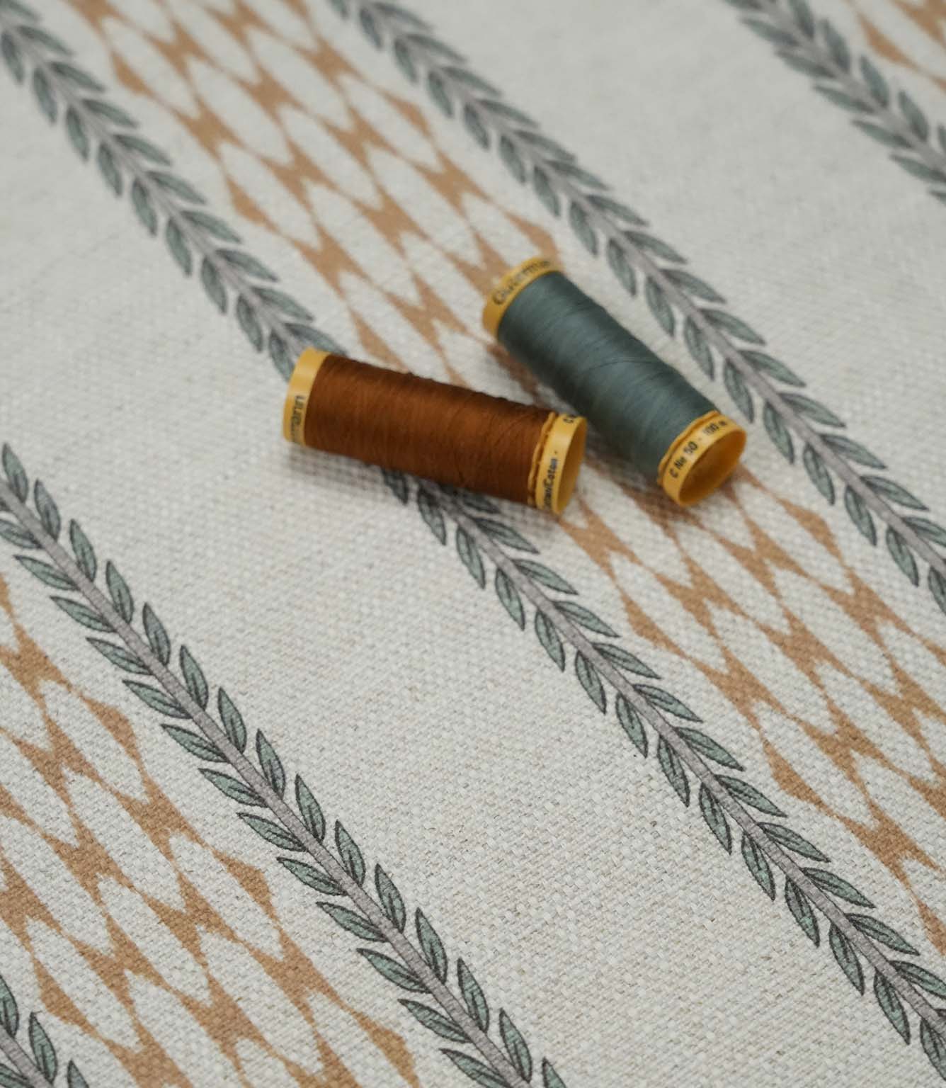 Varese Rust contemporary upholstery fabric with matching rust and sage thread reels highlighting the fabric texture and pattern scale.