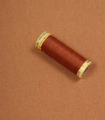 Spool of orange thread on a terracotta fabric background