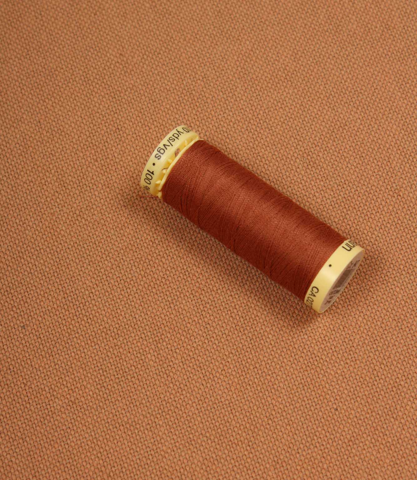 Spool of orange thread on a terracotta fabric background