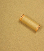 Spool of beige thread on a yellow fabric background