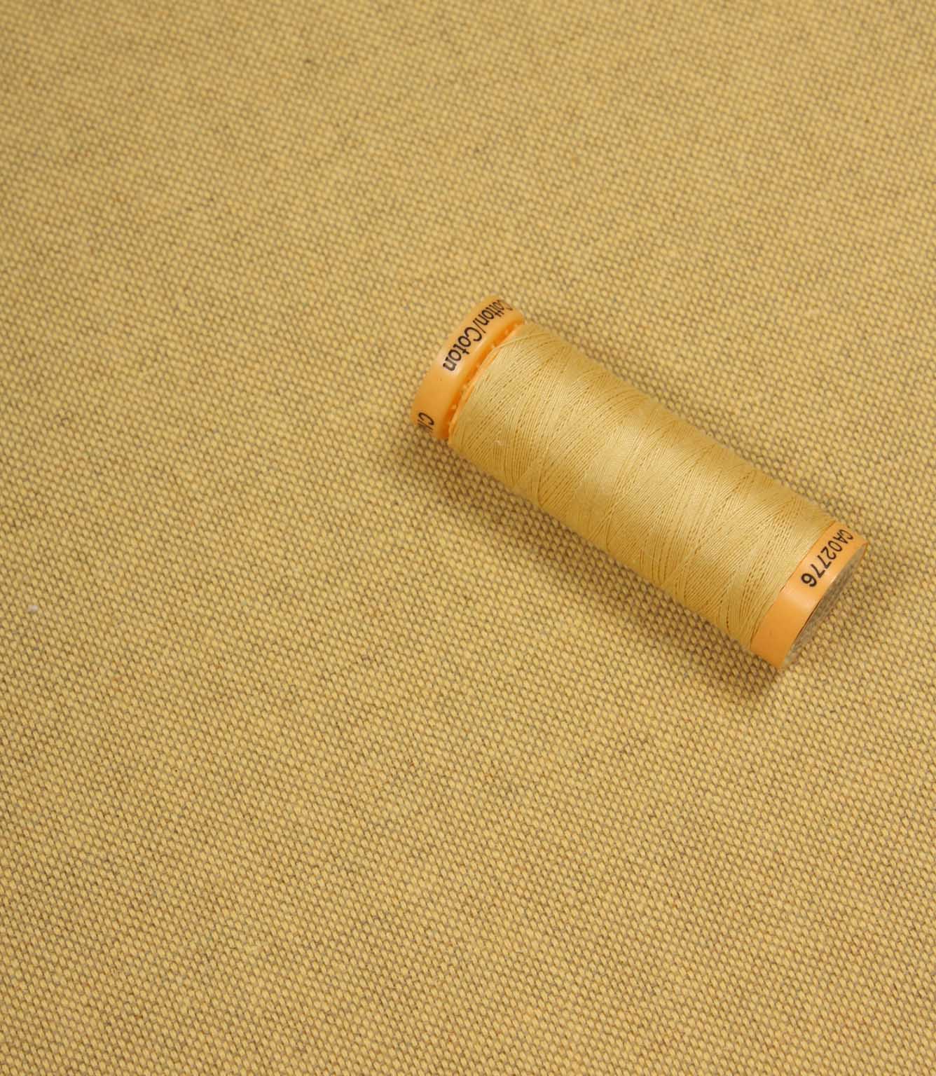 Spool of beige thread on a yellow fabric background