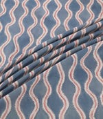 Wading Anemone fabric arranged in soft diagonal folds, showcasing its contemporary wave-inspired pattern in dusty blue, with cream scalloped edges, delicate red detailing and a subtly textured woven appearance.