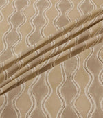 Wading Quaker fabric arranged in soft diagonal folds, showcasing its contemporary wave-inspired pattern in beige and taupe, with delicate cream scalloped borders, fine brown outlines and a subtly textured woven appearance.