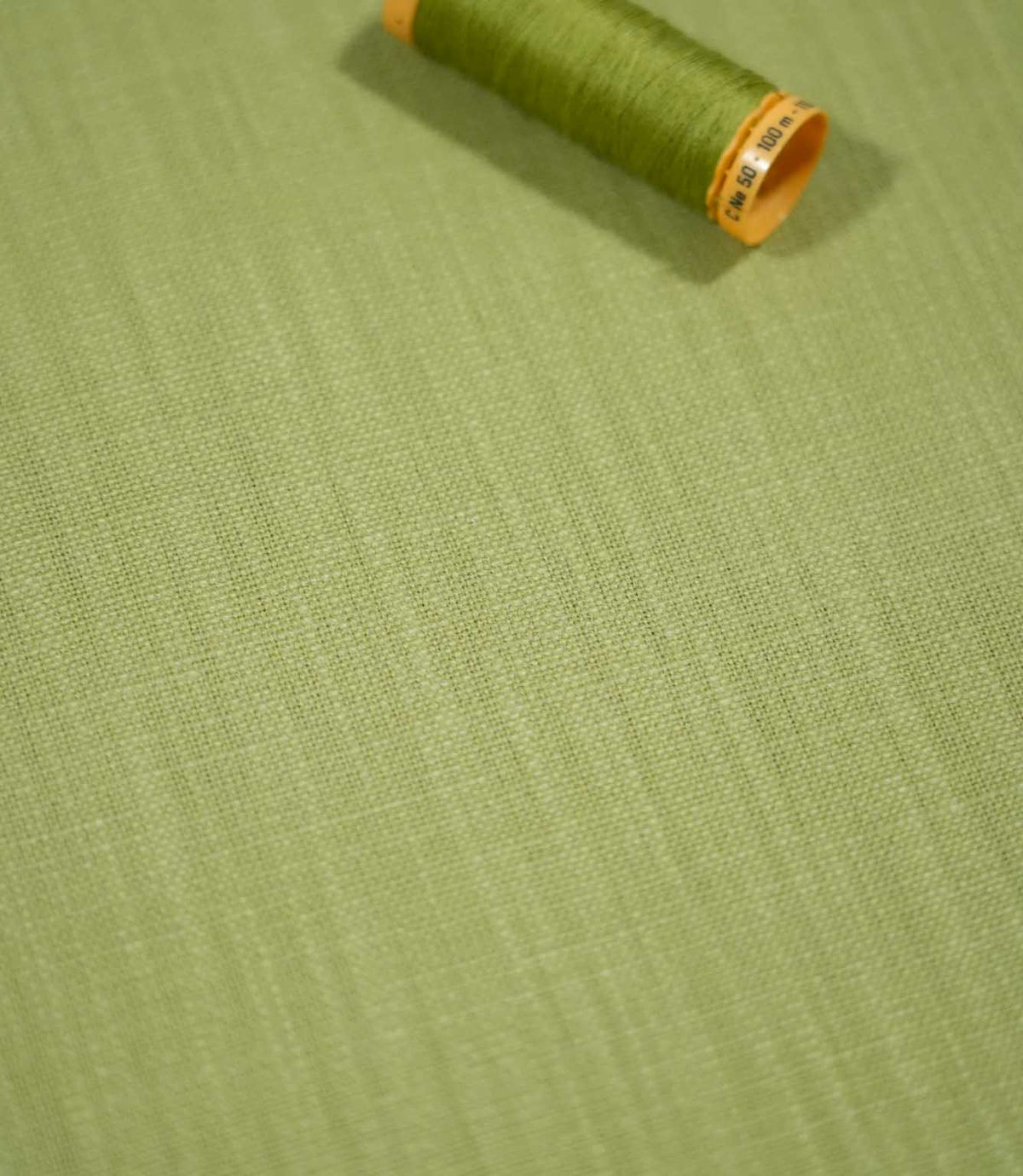 Waverley Celery green fabric laid flat with a coordinating thread spool, showing the subtle woven texture and soft green tones.