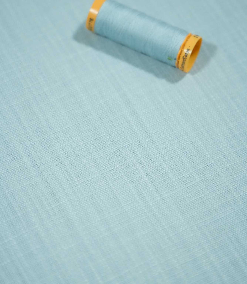 Waverley Duck Egg 100% brushed cotton fabric laid flat with a coordinating pale blue thread spool, highlighting its fine weave and soft blue-green colouring.