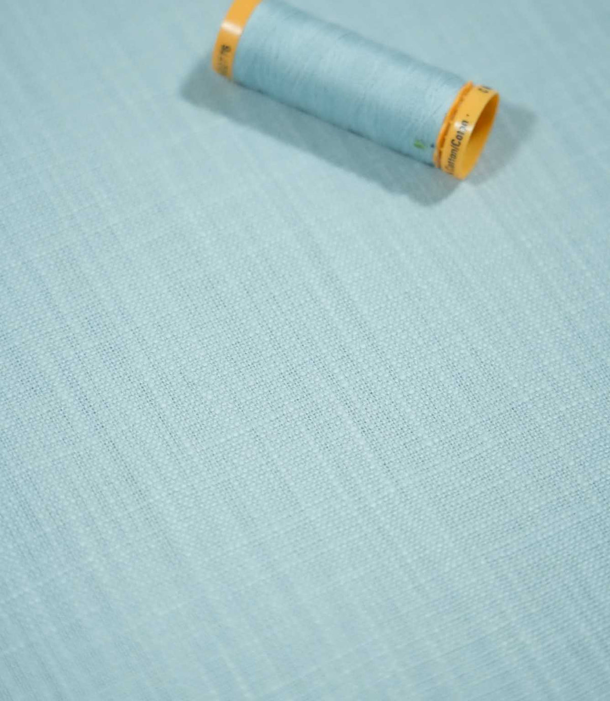 Waverley Duck Egg 100% brushed cotton fabric laid flat with a coordinating pale blue thread spool, highlighting its fine weave and soft blue-green colouring.