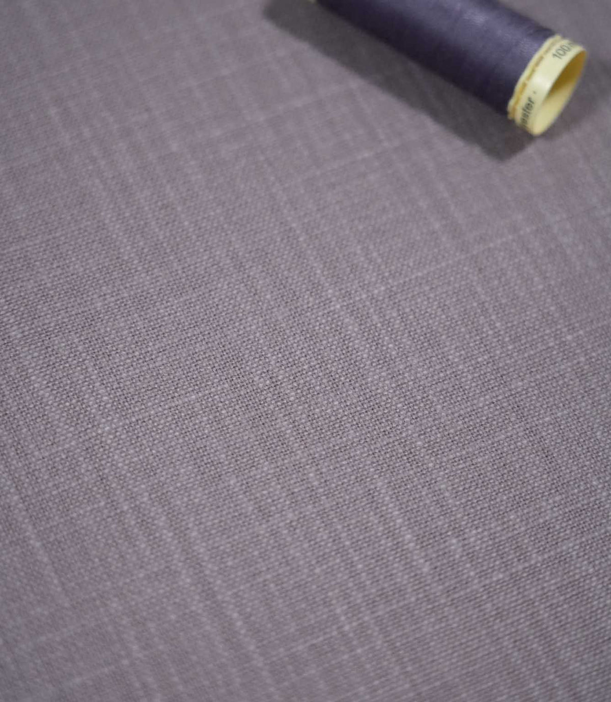 Waverley Heather brushed cotton fabric laid flat with a coordinating deep purple thread spool, highlighting its woven texture and muted lavender-grey colouring.