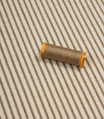 Wedmore Wide ivory striped fabric displayed with coordinating taupe thread spool, highlighting the fine embroidered stripe detail.