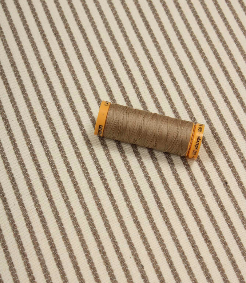 Wedmore Wide ivory striped fabric displayed with coordinating taupe thread spool, highlighting the fine embroidered stripe detail.