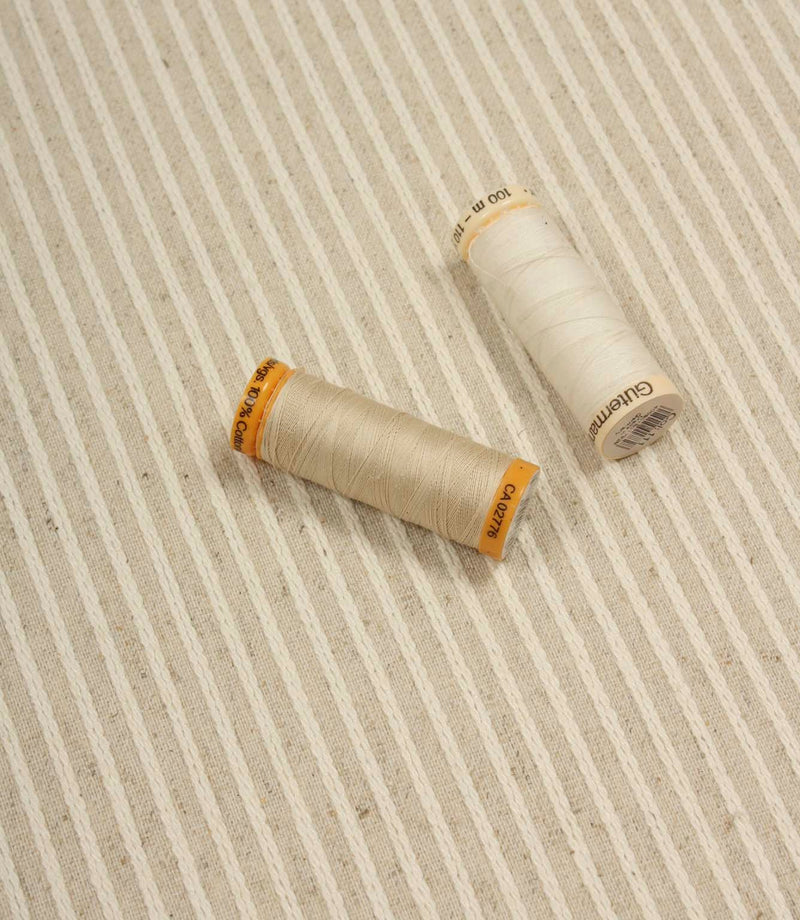 Wedmore Wide striped upholstery fabric displayed with coordinating thread spools, highlighting its woven texture and subtle stripe detailing.